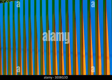Vertical striped fence in bold orange, blue and green tones creating a rhythmic geometric abstract background with vibrant, playful color and strong. Stock Photo