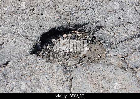 muddy pothole in cracked asphalt paved roadway in sunshine (macro, close-up) Stock Photo