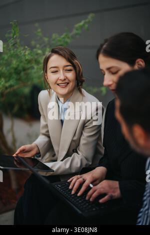 Three colleagues collaborating on a laptop and tablet during an outdoor business meeting Stock Photo