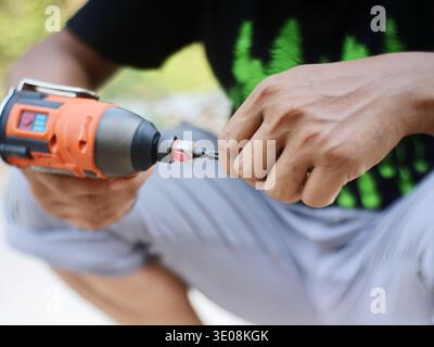 Mechanic changing or inserting a drill bit into an orange cordless impact drill. Stock Photo
