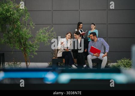 Business colleagues collaborating outdoors on a bench with laptop, tablet and documents Stock Photo