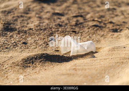 Discarded plastic cup lying on sandy beach symbolizing pollution and environmental problem Stock Photo