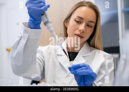 Performing precise pipetting technique to transfer red liquid samples into microcentrifuge tubes at laboratory workstation. Blood sample analysis Stock Photo
