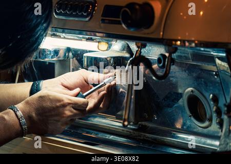 Technician skillfully using screwdriver removing nut from coffee maker on counterbar in coffee shop. Process service of equipment maintenance in bever Stock Photo