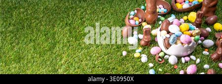 Easter egg hunting background with chocolate eggs. Various candy and chocolate Easter eggs, bunny and rabbits with basket for eggs on green grass park Stock Photo