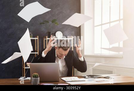 Young man sitting at table with papers flying around Stock Photo