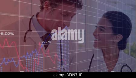 Smiling two doctors in lab coats exchanging look in clinic, showing stethoscopes and data graphs Stock Photo