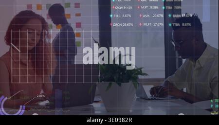Collaborating team of four typing in shirts at glass with sticky notes, laptops, overlays, tablet Stock Photo