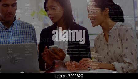 Collaborating three colleagues in office attire reviewing code overlay with laptop, smartphone, pen Stock Photo