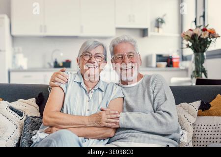 Happy mature husband and wife sit rest on couch at home hugging and cuddling, show care affection, smiling senior loving couple relax on sofa have fun Stock Photo