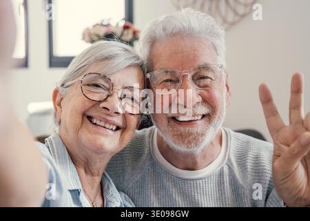 Head shot portrait happy senior couple taking selfie, having fun with phone cam, smiling aged wife and husband hugging, looking at camera, posing for Stock Photo