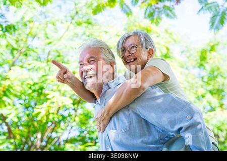 Two happy and cheerful senior, old man carrying on his back his wife having fun and laughing together. Bonding loving old family couple embracing, fee Stock Photo