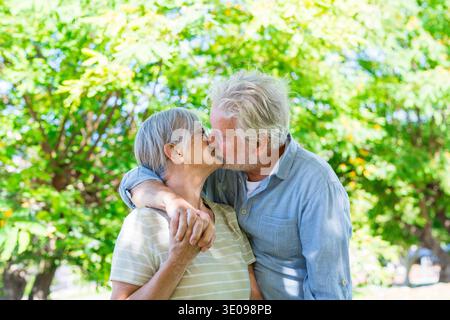 Beautiful cute couple of seniors hugged having fun and enjoying together outdoors in green park smiling and relaxing. Two pensioners embracing taking Stock Photo
