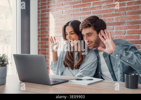 Happy young couple laughing watching funny video or comedy movie online, cheerful man and woman having fun enjoying videocall looking at laptop screen Stock Photo