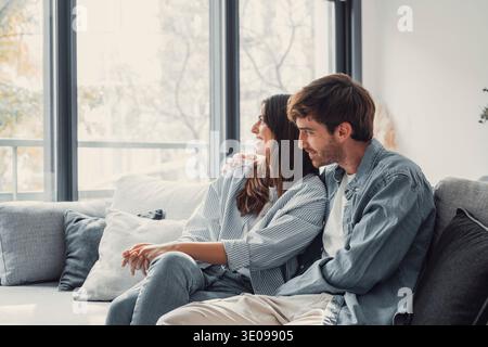 One dream for two of us. Romantic millennial spouses relax on couch together looking aside imagining happy future life. Young man and woman in love cu Stock Photo