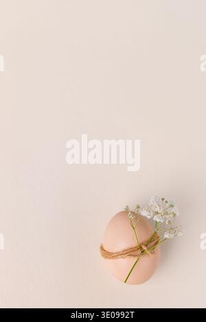 An egg wrapped with twine and adorned with small white flowers, placed on a soft pastel background, creating a minimalist aesthetic easter bavkground Stock Photo