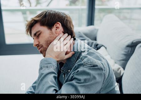 Upset tired young man feeling pain massaging stiff neck rubbing tensed muscles to relieve back ache joint shoulder discomfort after long sedentary wor Stock Photo