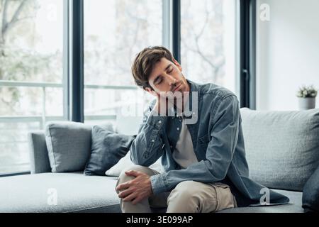 Upset tired young man feeling pain massaging stiff neck rubbing tensed muscles to relieve back ache joint shoulder discomfort after long sedentary wor Stock Photo