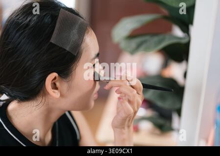 Closeup portrait of attractive asian female getting ready applying cosmetics, brush for facial makeup, dialy grooming, cosmetic application and self c Stock Photo
