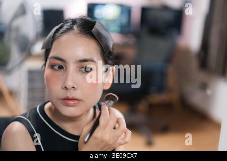 Closeup portrait of attractive asian female getting ready applying cosmetics, brush for facial makeup, dialy grooming, cosmetic application and self c Stock Photo