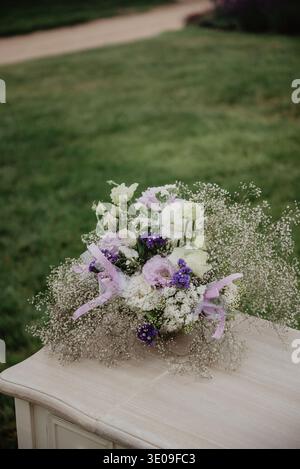 Delicate pastel flower arrangement featuring roses, lisianthus and baby's breath in a rustic pot on a wooden table outdoors. Soft natural light and ga Stock Photo