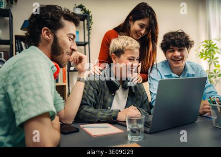 A happy and diverse creative team collaborates around a laptop in a modern startup office, expressing positive workplace culture, teamwork, and inclus Stock Photo