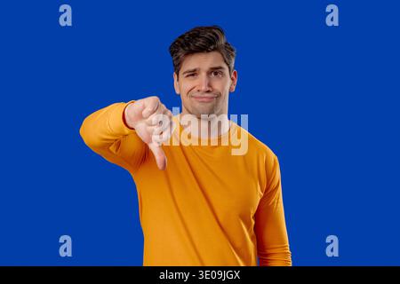 Handsome man In Yellow Wear Giving Thumbs Down Dislike With Disapproving Look Stock Photo