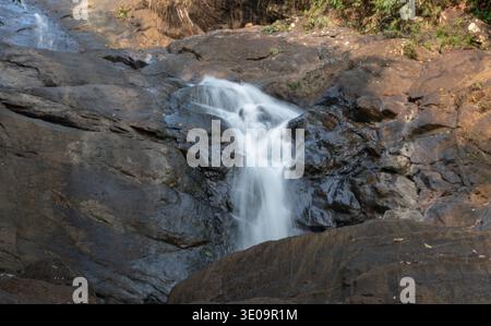 A beautiful, small cascade of the  Ella waterfall flows over dark, rugged rocks, surrounded by lush green vegetation in Sri Lanka Stock Photo
