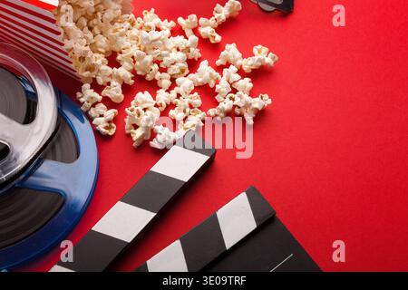 Clapperboard, film reel and popcorn on red background Stock Photo