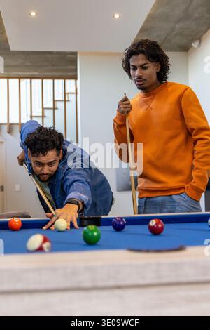 Indian friends playing pool in home rec room, leaning and lining up shot on blue-felt table Stock Photo