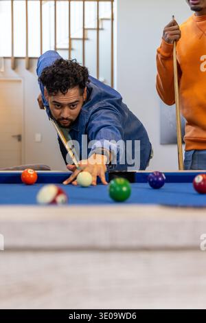 Diverse males lining up pool shot at blue felt table in home with cues, billiard balls Stock Photo