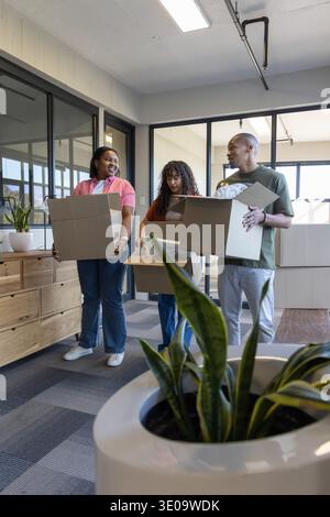 Diverse coworkers carrying cardboard boxes while unpacking near white planter at office windows Stock Photo