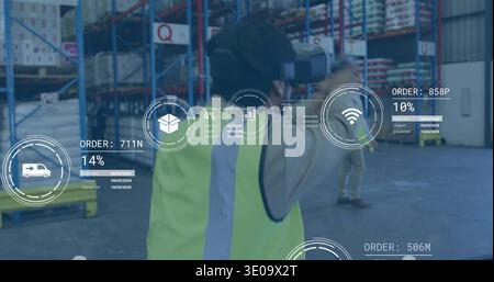Interacting Asian worker in yellow hi-vis vest and VR headset gesturing at AR overlays in warehouse Stock Photo
