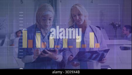 Reviewing nurse in headscarf and doctor examining X-ray at nurses' station, with tablet overlay Stock Photo
