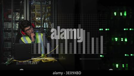 Tech wearing hivis-vest and red muffs testing servers and yellow cables at data center with laptop Stock Photo