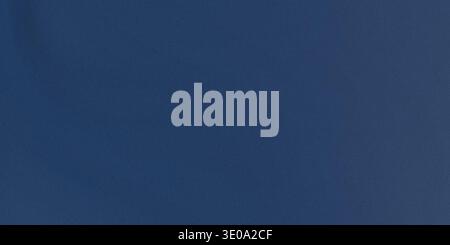 A close-up view of a dark blue fabric texture with a smooth surface, showing its uniform color and subtle sheen, with a slight gradient effect Stock Photo