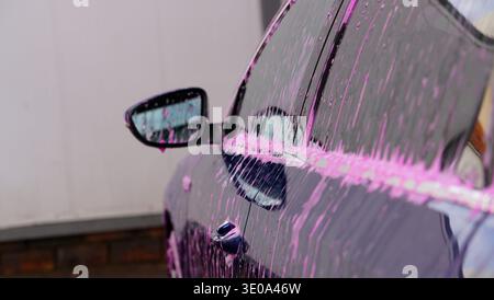Car covered with pink foam during washing close up side view Stock Photo