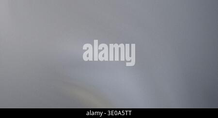 A close-up of a silver or light gray textured surface, possibly brushed metal, showing fine grain and a soft, diffused light reflection near the botto Stock Photo