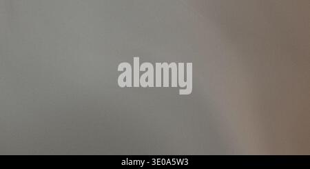 A detailed shot of a neutral gray surface, possibly brushed metal or a fine textile. The lighting creates a gentle, warm gradient from the left to the Stock Photo
