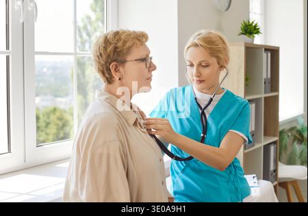 Female nurse performing stethoscope examination on senior patient in modern clinic Stock Photo