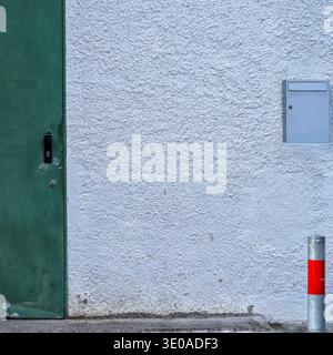 Minimalist urban, weathered green door, textured white wall, metal mailbox, and a red-striped bollard. Stock Photo