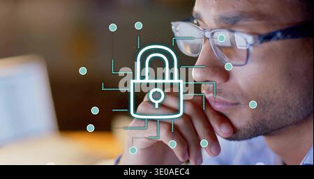 Analyzing Hispanic man wearing blue shirt and glasses, resting chin at desk with padlock overlay Stock Photo