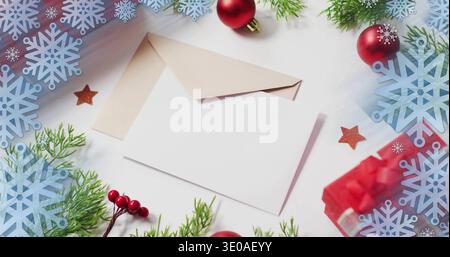 Displaying blank white greeting card resting atop open kraft envelope on tabletop, with red bauble Stock Photo