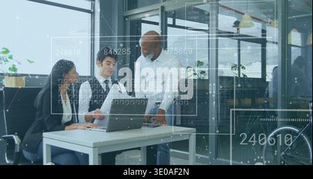 Discussing three coworkers in office attire analyzing laptop with data overlays at office desk Stock Photo