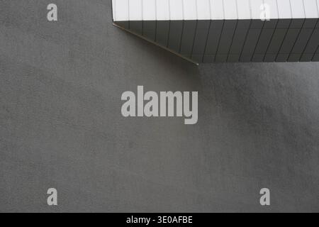 Modern architecture, detail, intersection of a textured gray concrete wall and a geometric white overhang. Stock Photo