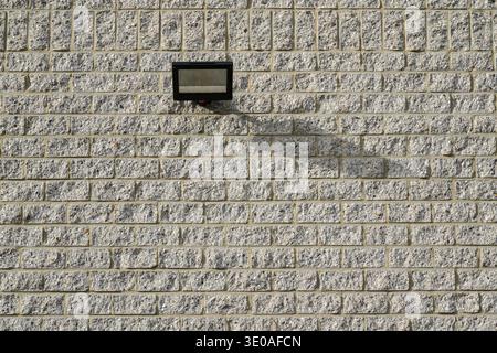 Modern architectural detail. A minimalist gray brick wall featuring a single, rectangular black lamp casting a subtle shadow. Stock Photo