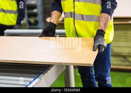 Worker processing wood board on conveyor in factory Stock Photo