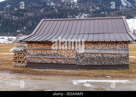 Large pile of split timber for heating stored by a rural barn in the winter mountain peaks Stock Photo