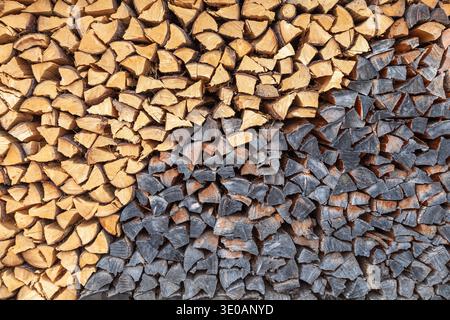 Contrast of fresh and weathered split firewood logs stacked in a textured background wall Stock Photo