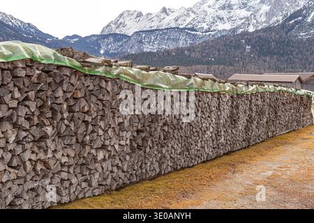 Extremely long woodpile of split logs covered with green tarp in a rural Alpine mountain field Stock Photo